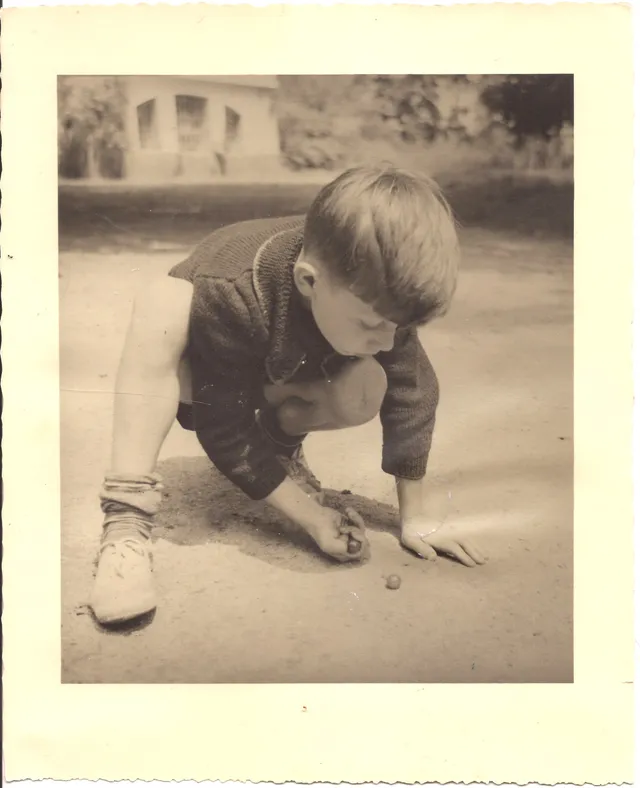 Photographie ancienne en noir et blanc d'un enfant jouant aux billes